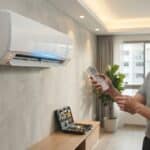 A professional technician diagnosing a blinking orange timer light on an indoor Panasonic split air conditioner unit using a remote controller in Singapore.