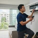 A professional HVAC technician inspecting an inherited wall-mounted air conditioning unit in a Singapore resale HDB flat to evaluate keeping, overhauling, or replacing the system.
